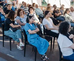 Plateia a assistir a um evento ao ar livre, sobre mulheres refugiadas em Portugal.