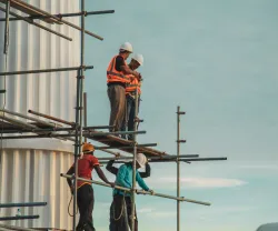Imagem de trabalhadores da construção civil num andaime de um prédio em construção.