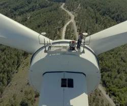 Vista de cima de uma turbina eólica, com duas pessoas na plataforma de manutenção.