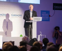 O professor Dani Rodrick a discursar, num púlpito, para uma plateia. Fundo com o logo da Fundação.