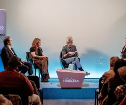 Quatro pessoas em destaque num painel, com o texto "PRAÇA da FUNDAÇÃO" em primeiro plano.
