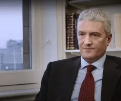 Homem com cabelo grisalho, no caso o professor Francisco Bethencourt, sentado em frente a uma janela, com prateleira de livros atrás.