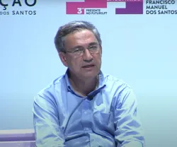 Orhan Pamuk sentado num banco. Fundo branco com o logotipo da Fundação.