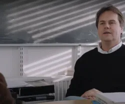 O astrofísico Pedro Ferreira sentado, numa sala de aula. Ao fundo, reflexos de luz no quadro.