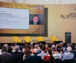 Plateia a olhar para uma tela na qual se vê David Autor a falar. Texto: "Desafiar Portugal". 