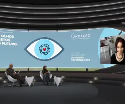 Um homem e uma mulher sentados, num estúdio de televisão, a olhar para uma tela, na qual está Elissa Epel a falar. Do lado oposto da tela lê-se "De olhos postos no futuro". 
