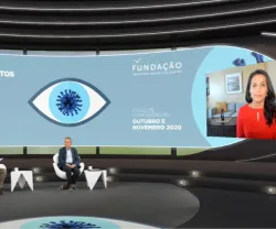 Dois apresentadores sentados, num estúdio, a olhar para uma tela na qual se vê Nahid Bhadelia a falar