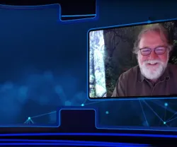 Sean B. Carroll, com barba e óculos, sorri durante uma videoconferência com fundo natural.