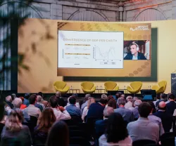 Conferência com várias pessoas a olhar para uma tela na qual Thomas Philippon está discursar.