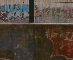 Mulher a passear com um bebé ao colo, enquanto empurra um carrinho, ao lado de uma parede com graffitis.