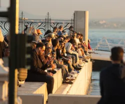 Pessoas de várias idades estão sentadas junto ao rio tejo, em Lisboa, ao entardecer. Crédito: Shutterstock