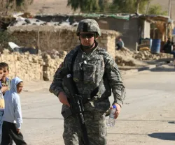 em grande plano um soldado norte-americano junto a uma estrada no Iraque, enquanto ao fundo várias crianças apontam para o militar. Crédito: Shutterstock