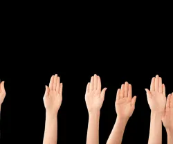 várias mãos no ar, sob um fundo preto, mostrando participação eleitoral. Crédito: Canva