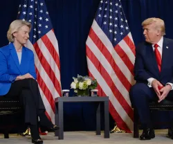 Ursula von der Leyen sentada ao lado de Donald Trump, com duas bandeiras dos EUA atrás.
