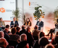 Uma plateia sentada, de costas, a olhar para um palco onde estão quatro oradores, entre eles Pedro Passos Coelho e Elvira Fortunato.