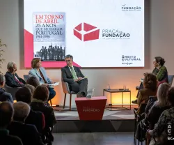 Quatro pessoas sentadas num palco. Atrás, um ecrã com a capa de um livro da Fundação e com o texto "Praça da Fundação".