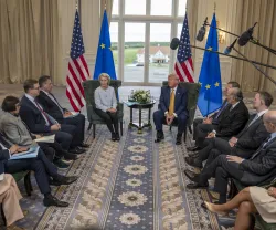 Ursula von der Leyen sentada ao lado de Donald Trump, com bandeiras da UE e dos EUA.