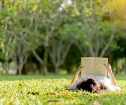 Uma rapariga jovem está a ler deitada na relva de um parque. Crédito: Shutterstock