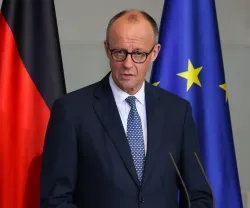 Retrato a cores de um homem com óculos, o chanceller alemão Merz, à frente de duas bandeiras: uma da Alemanha a outra da UE. Créditos:shutterstock.