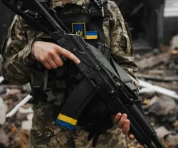 Um soldado carrega uma arma ao peito, com a bandeira ucraniana destacada no seu colete de proteção. Créditos: shutterstock