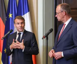 Emmanuel Macron e Friedrich Merz, lado a lado, durante uma conferência de imprensa conjunta. Bandeira de França, Alemanha e da UE ao Fundo. Créditos: shutterstock