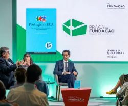 Imagem de quatro pessoas a conversar perante uma plateia,  sob um fundo verde.
