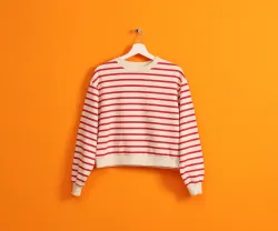 Imagem de uma camisola branca com riscas pendurada num cabide, sob fundo cor de laranja. Crédito: Shutterstock.