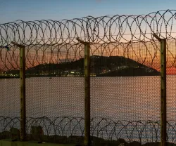 Ceuta, cidade espanhola no norte da África, vista do Marrocos atrás de uma cerca de arame espinhoso localizada na fronteira marroquina, contra um deslumbrante pôr do sol sobre o mar. Crédito: Shutterstock