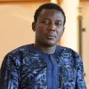 Escritor e linguista nigeriano Kọ́lá Túbọ̀sún, sentado tendo como fundo uma parede em tons laranja. Crédito: Faberllull