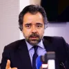 Imagem de um homem sentado, num estúdio de rádio, com um microfone à frente.
