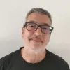 Retrato de um homem de óculos e camisola preta. Fundo claro.