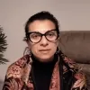 Imagem de uma mulher sentada num sofá, com uma planta ao lado.