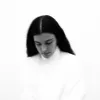 Imagem a preto e branco da artista Silly, a olhar para baixo e vestida de branco.