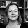 Retrato a preto e branco da socióloga Tatiana Moura. Uma estante com livros e fotografias a cobrir o fundo.