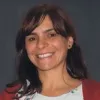 Imagem de uma mulher sorridente, vestida com uma camisola com um padrão e um casaco vermelho.