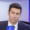 Imagem de um homem sentado, a falar para um microfone, num estúdio de rádio.
