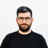 Imagem de um homem, com barba, e de óculos. Vestido com uma t-shirt preta.