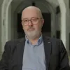 Retrato de um homem careca, com óculos, vestido com um fato de camisa azul e casaco preto.
