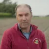 Retrato a cores de um homem, vestido com um casaco vermelho onde se lê "Batata-doce de Aljezur». Um campo agrícola cobre o fundo.