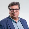 Retrato a cores de um homem, de óculos, com expressão sorridente. Veste uma camisa azul. Créditos: Reinaldo Rodrigues