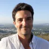 Retrato a cores de um homem a sorrir sobre uma paisagem. 