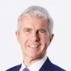 Retrato a cores de um homem de olhos azuis e expressão sorridente. Tem cabelo branco. Fundo cinzento claro.