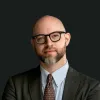 Retrato a cores de um homem sobre um fundo preto. Tem barba, usa óculos e um fato. Créditos: Foreign Policy