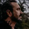 Imagem de perfil de um homem de barba, com tatutagens no pescoço, o músico Fernando Ribeiro, fundador dos Moonspell
