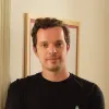 Imagem de um homem, o maestro Martim Sousa Tavares, vestido com uma t-shirt preta sob um fundo bege.